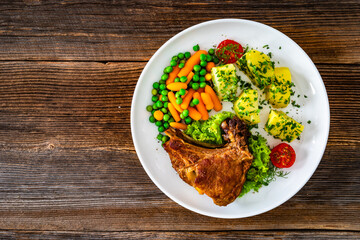 Baked veal cutlet with bone, boiled potatoes, mini carrots and green peas on wooden table