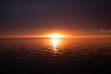 Golden sunset over calm sea with vivid reflections on the water, dramatic sky, and serene horizon, creating a peaceful and atmospheric seascape.