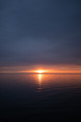 Serene sunset over calm sea with glowing orange horizon, soft reflections on the water, and dramatic evening sky, creating a peaceful and atmospheric seascape.