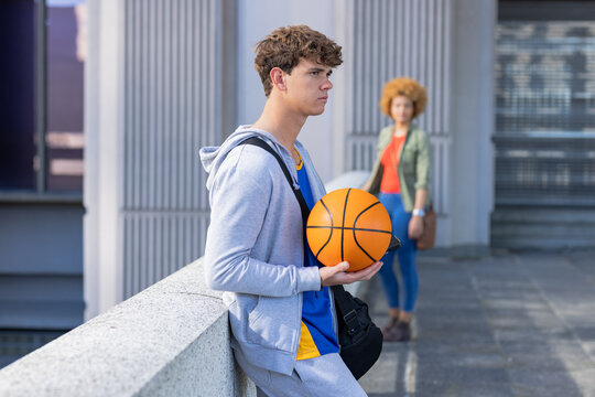 Friends leaning on concrete parapet at roof terrace carrying basketball, sports bags, copy space