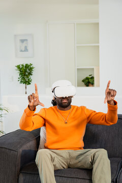 VR headset is resting on gray sofa in living room, with white shelves featuring potted plants