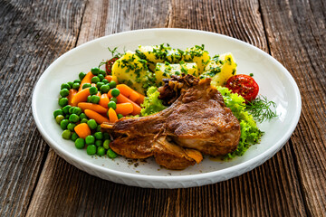Baked veal cutlet with bone, boiled potatoes, mini carrots and green peas on wooden table