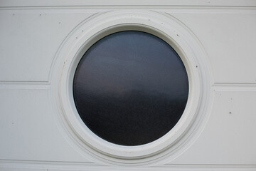 Close-up of a round porthole-style window with a black center set in a white textured surface, resembling nautical or modern architectural design details.