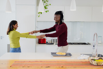 Diverse couple holding hands at modern kitchen island with baking sheet, red toaster, chrome faucet