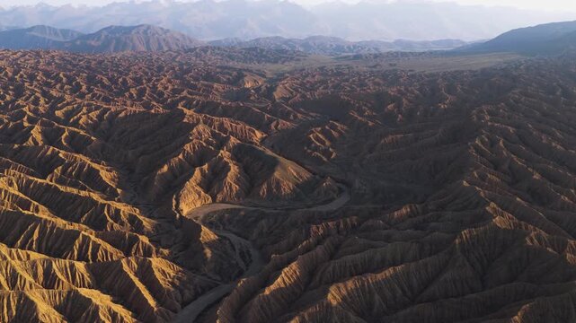 Aerial view of the arid landscape, displaying brown geological formations and a winding river cutting through the terrain, Ak Say, Issyk-Kul Region, Kyrgyzstan.