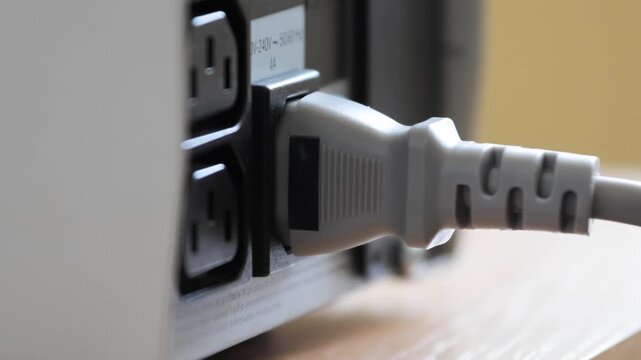 Close-up of power cable being connected to uninterruptible power supply unit. Image shows hand inserting plug into socket on UPS for secure electrical connection during equipment setup.
