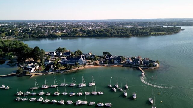 Aerial view of boats anchored in tranquil waters near a peninsula with houses, contrasting with the distant city, Presqu'&icirc;le de Conleau, Vannes, Bretagne, France.