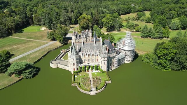 Aerial view of the majestic La Bretesche castle surrounded by a moat, lush green trees, and sprawling grass, Missillac, Pays de la Loire, France.