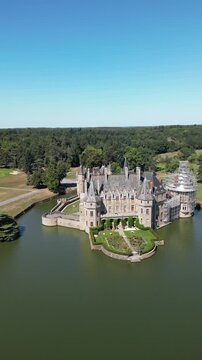 Aerial view of the grand Chateau de la Bretesche, encircled by a tranquil moat reflecting the clear sky, a historic jewel, Missillac, Pays de la Loire, France.
