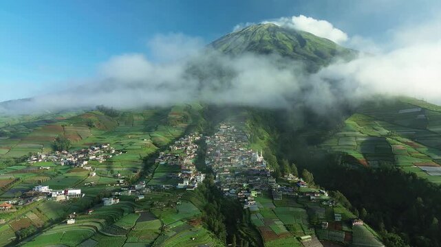 Aerial view of Nepal Van Java village nestled among vibrant green terraced hills and a majestic mountain partially shrouded in clouds, Magelang, Central Java, Indonesia.
