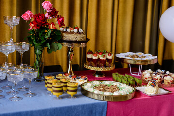 A lavish and colorful dessert buffet featuring a chocolate berry cake, an assortment of fine pastries, and a tower of champagne glasses, beautifully arranged for a luxurious wedding reception or celeb