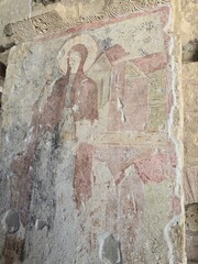 Faded fresco of haloed figure with medieval architecture on ancient stone wall