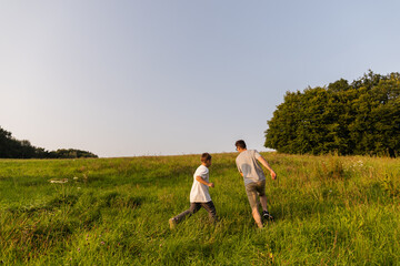 A father and son are enjoying their time outdoors, running together through a lush green field...