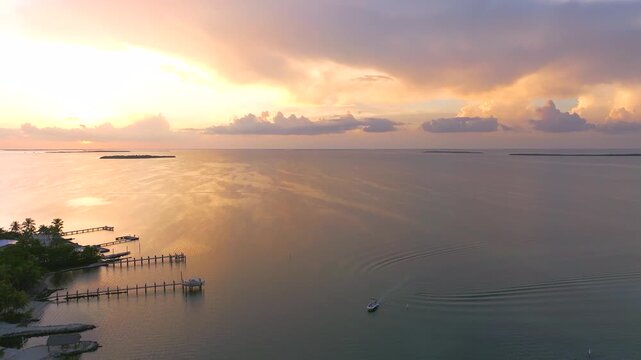 Aerial view of piers stretching into the tranquil water, and a single boat sailing under a multicolored sunset sky, Key Largo, Florida, United States.