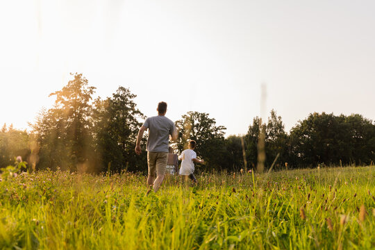A father and his son run together through a lush green field during golden hour. Sunlight makes the scene warm and inviting as they share laughter and bonding moments