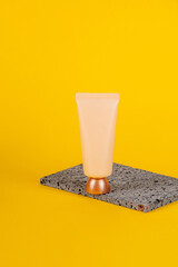 Cosmetic product in tube, bottle, lotion or serum with stylish props on yellow background. 