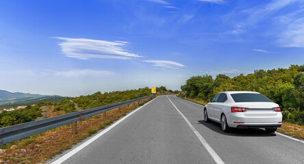 A white car drives along a winding mountain road surrounded by greenery and scenic views under a...