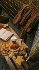 Autumn picnic scene on a park bench with a croissant and coffee.