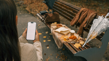 Woman holding a smartphone with a blank screen in an autumn park.