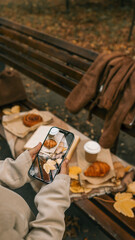 Autumn picnic scene with croissant and coffee being photographed on a park bench.
