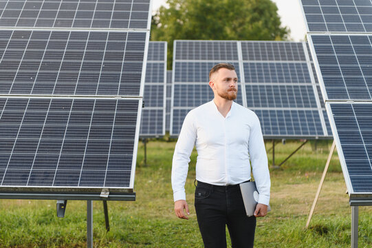 Engineer holding laptop walking among solar panels