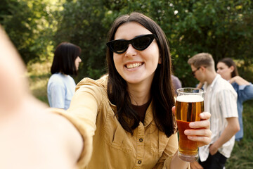 Young woman with beer taking selfie at party outdoors