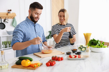 Smiling woman opening bottle of wine while cooking with her husband at table in kitchen