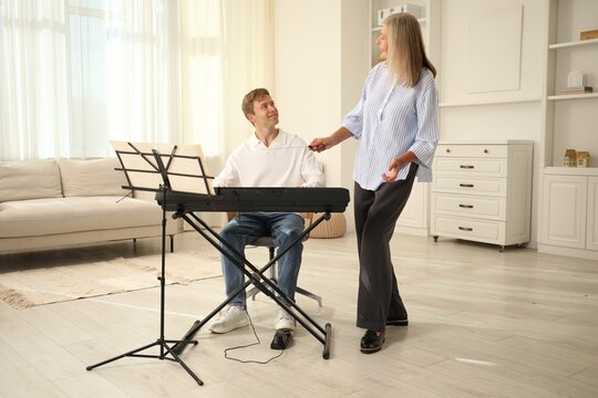 Tutor teaching man to play piano indoors - Powered by Adobe