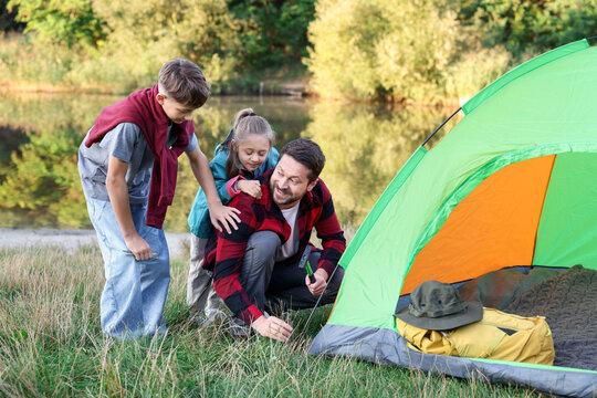Happy father and his children setting up camping tent near river outdoors - Powered by Adobe
