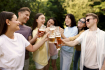 Blurred view of happy friends clinking glasses of beer outdoors