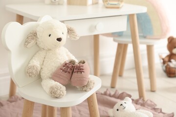 Cute soft toy sheep and baby shoes on chair indoors