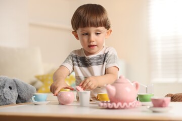 Cute little boy playing tea party with his toy elephant at table indoors