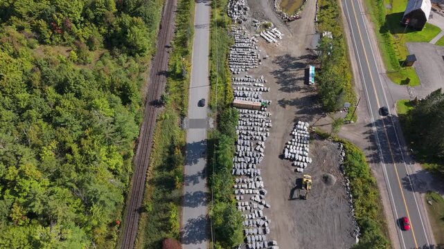 A top-down drone shot over Gravenhurst showing parallel roads, a railway, a stone supply yard, vehicles passing, and surrounding trees