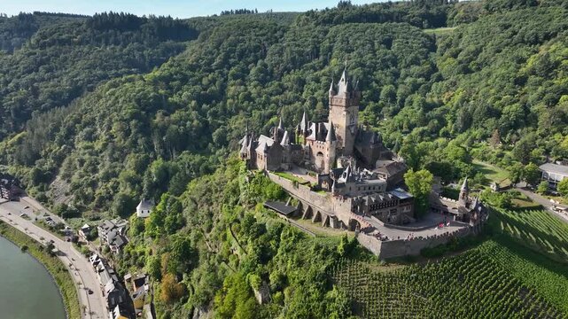 Aerial orbit of Reichsburg Cochem castle in Moselle Valley, Germany. Medieval castle sits on hilltop overlooking river and surrounded by vineyards and forests in Moselle Valley, Germany.
