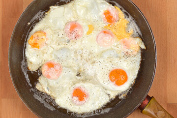 A top-down shot of several fried eggs sizzling in a pan on a wooden surface