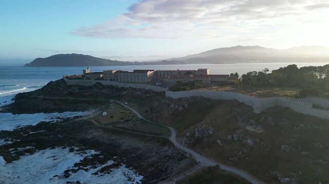 Aerial view of the historic Monterreal Fortress standing tall against the crashing waves, contrasting the rugged coastline, Baiona, Pontevedra, Spain.