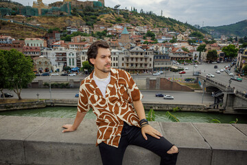 A male tourist poses from a viewing platform with the old town of Tbilisi in Georgia in the background.
