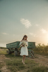 Young woman in white dress walking with daisies at sunset