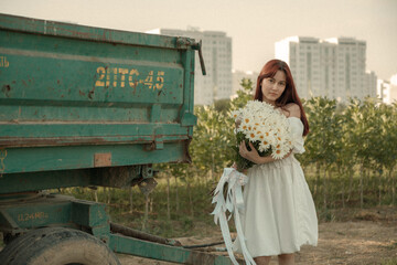 Young woman in white dress walking with daisies at sunset