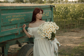 Young woman in white dress walking with daisies at sunset