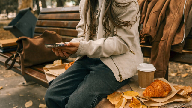 Person enjoying a relaxing autumn day with coffee and a croissant in the park.