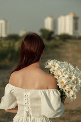 Photograph of a fair-skinned woman with long auburn hair, holding white daisies, outdoors. retro grain effect