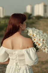 Photograph of a fair-skinned woman with long auburn hair, holding white daisies, outdoors. retro grain effect