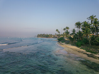 Aerial view of turquoise waves gently lapping against the sandy shore lined with swaying palm trees, a tropical haven of serenity, Weligama, Sri Lanka.