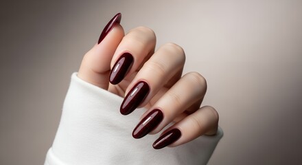 Close up view of a woman's hand showcasing perfectly manicured oval nails with dark red glossy polish against a soft gradient background and white fabric cuff Beauty Fashion Elegance