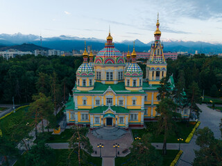 Aerial view of the Ascension Cathedral's vibrant domes and golden spires pierce the skyline amidst the green expanse of Panfilov Park, Almaty, Almaty Region, Kazakhstan.