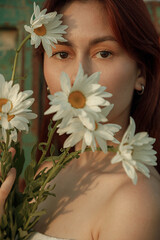 Close up portrait of young woman with bouquet of daisies outdoors