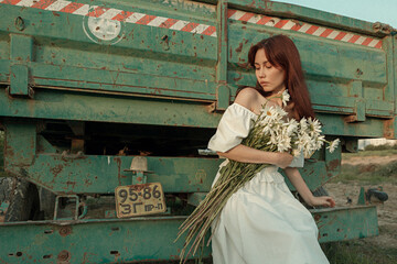Thoughtful young woman with daisies sitting by farm trailer.Retro grain effect