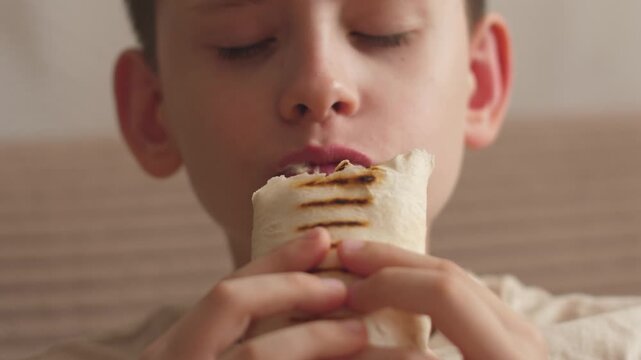 Caucasian happy teenager eating shawarma close-up, 11 year old boy eating fast food