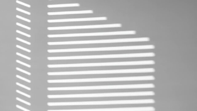 Abstract background of sunlight casting window blind shadows on a gray wall.